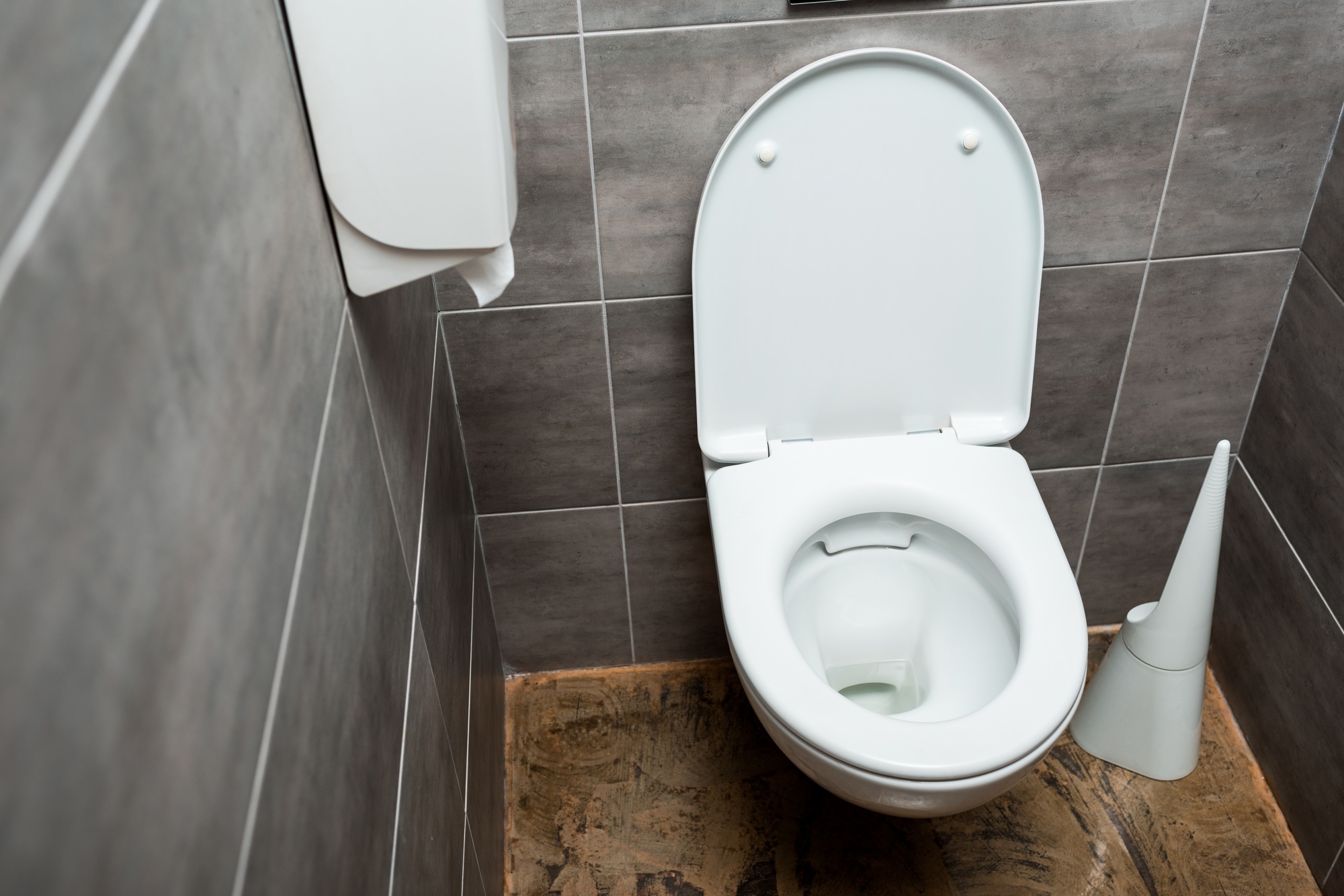 ceramic clean toilet bowl in modern restroom with grey tile and toilet brush