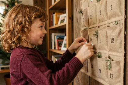 Fillette ouvrant une poche d'un calendrier de l'avent artisanal en tissu accroché à un mur en bois rustique